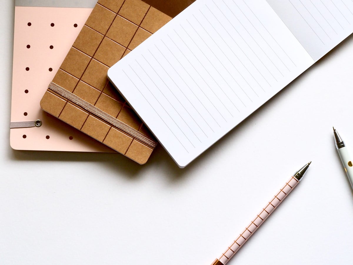 A white table with three notebooks and two pens