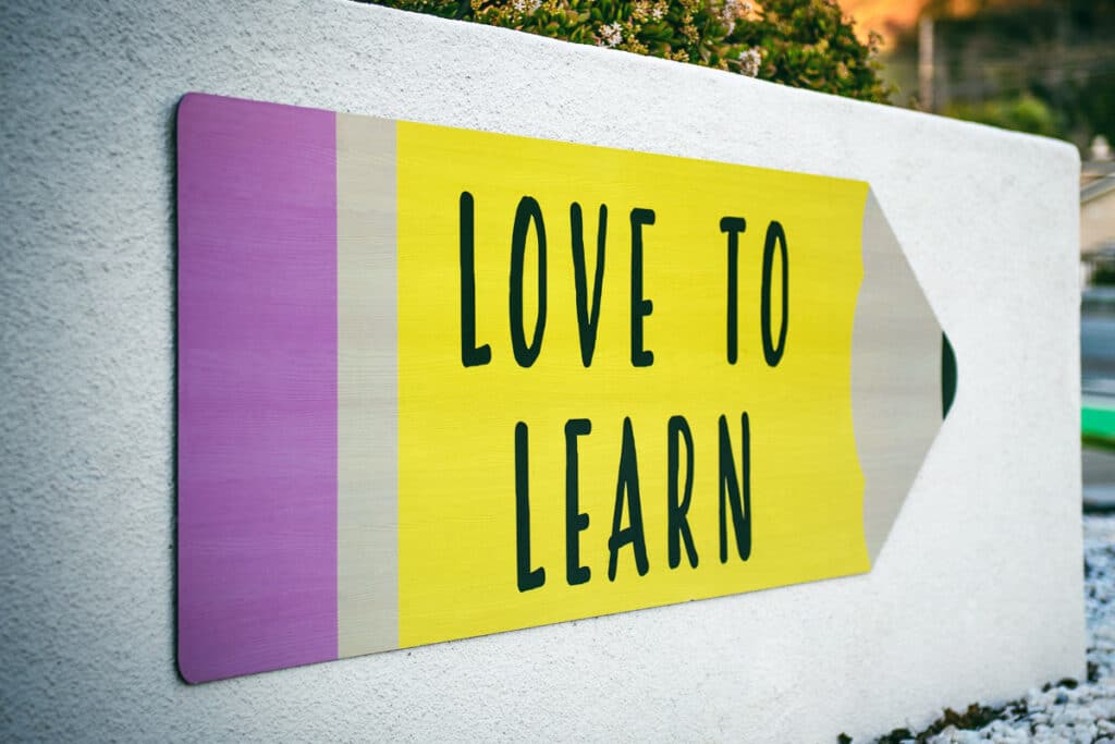 A white wall with a big colorful pencil with the words - love to learn on it