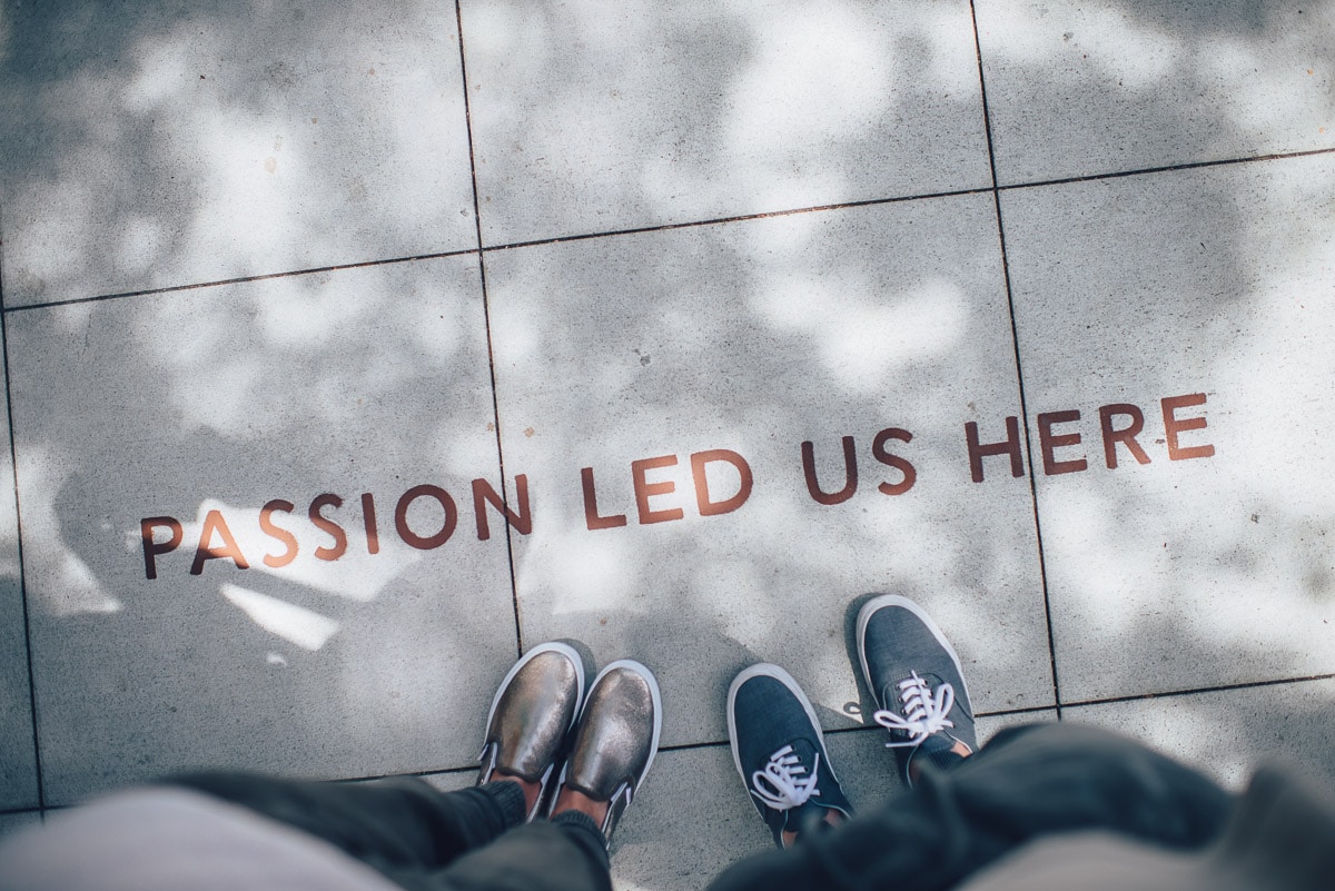 two people's feet looking down at a saying "passion led us here" on the ground