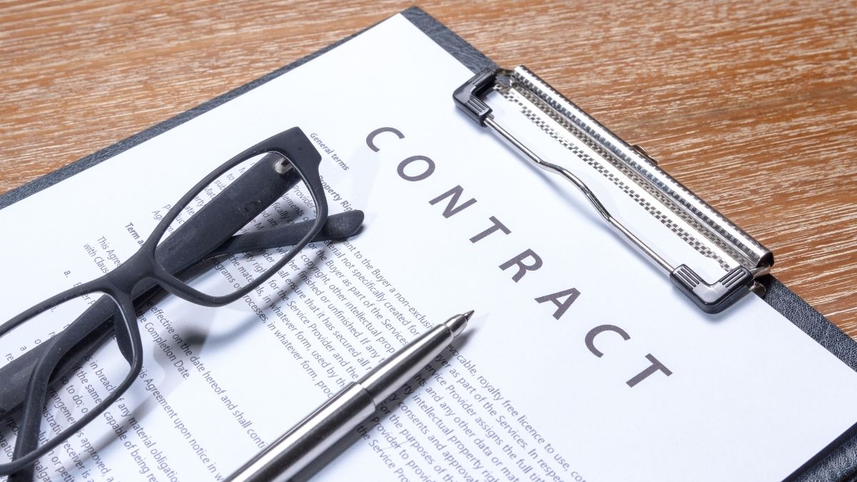 A clipboard with a contract on it with a pen and pair of glasses