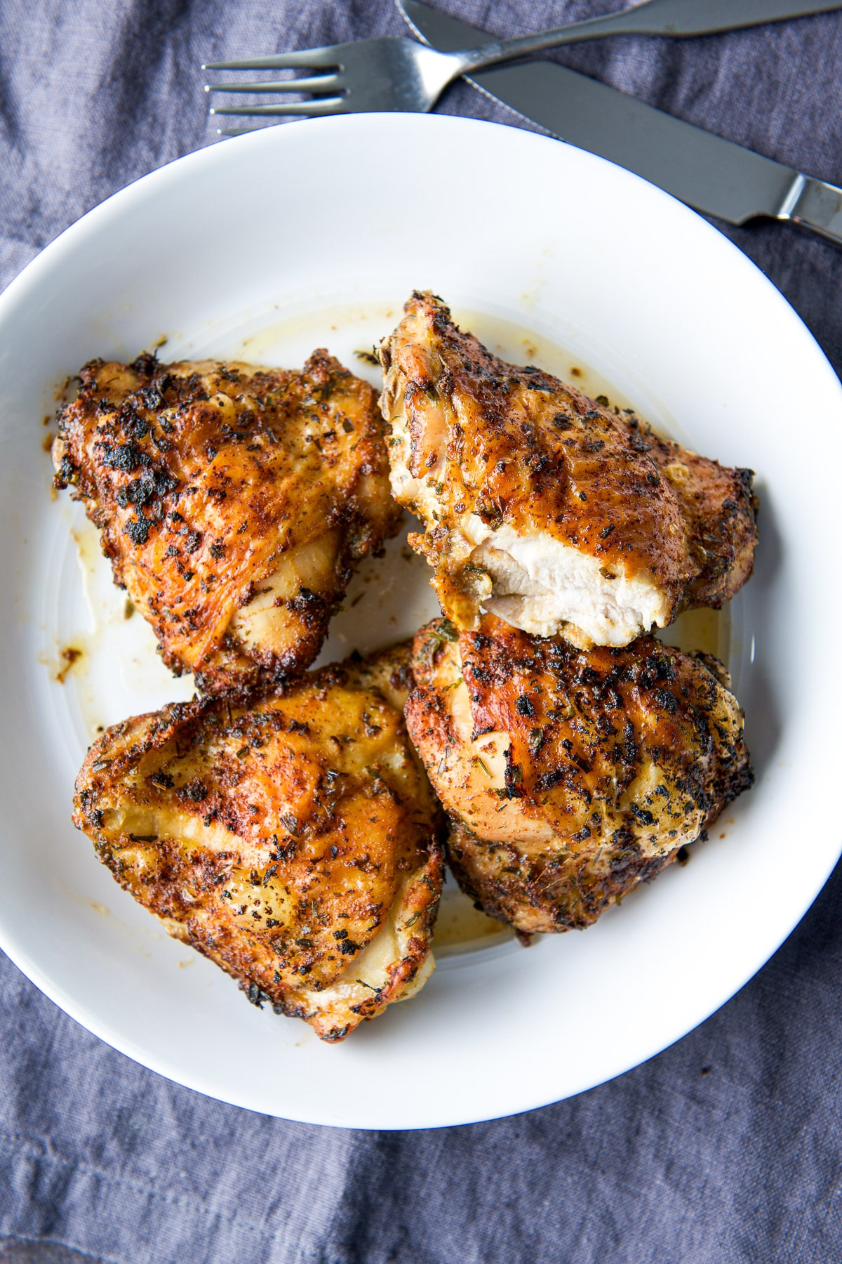 Overhead view of four chicken thighs in a white bowl with a slice out of one of them