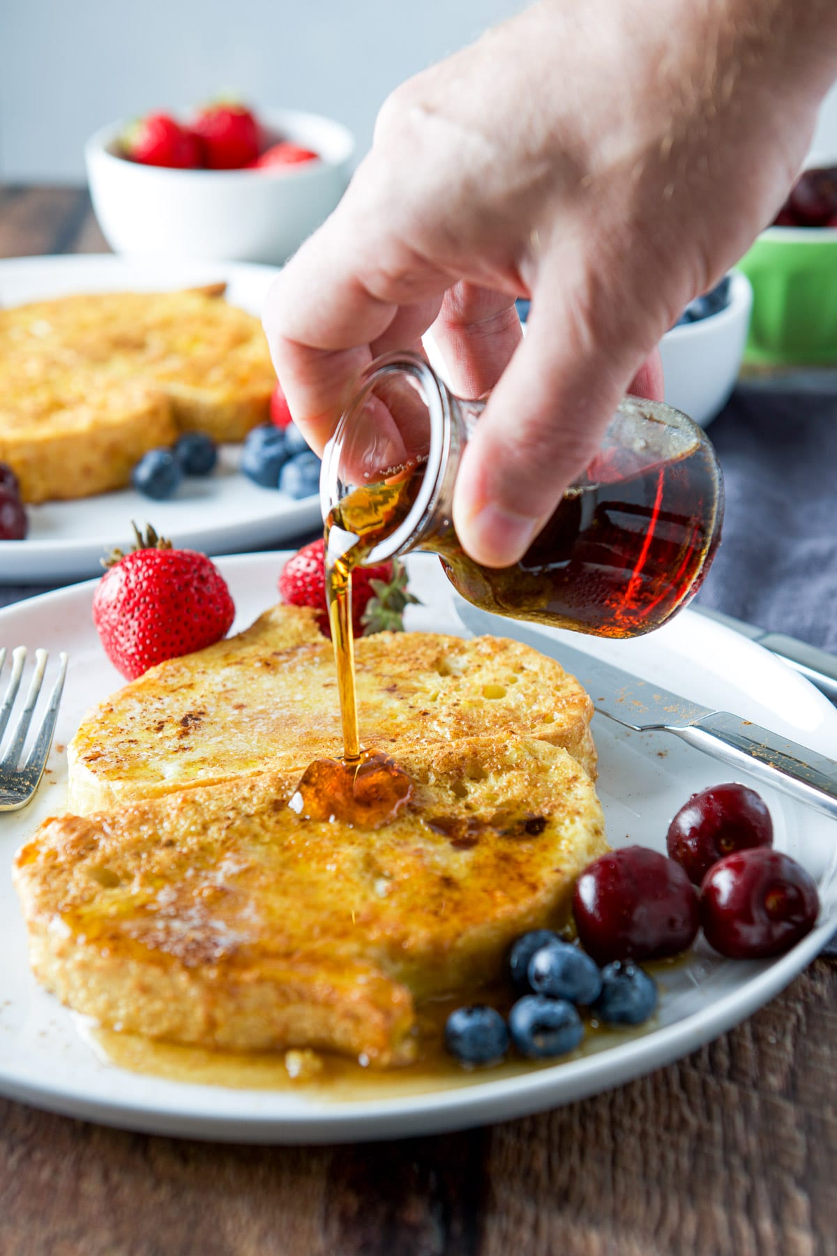 A male hand pouring syrup on some French toast