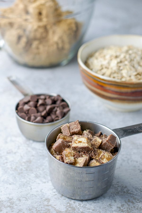 snickers bar cut up, chocolate chips, oats and the dough, all in measuring cups or bowls